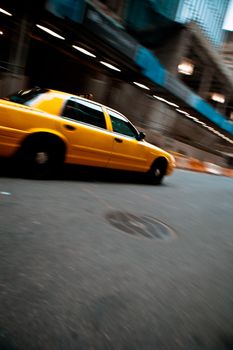 Pnned motion blur of a city street scene with a yellow taxi cab speeding by. 