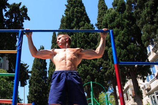 Young strong teenage athlete doing pull-up on horizontal bar