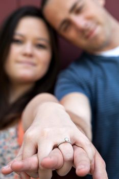 Young happy couple holding hands and showing the diamond engagement ring.  Shallow depth of field with strongest focus on the ring.