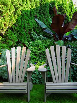 A photograph of a pair of wooden lawn chairs located in a garden.