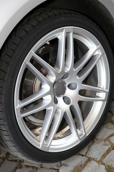 Alloy sportscar wheel detail showing the rim, hub, spokes and tyre parked on cobblestones