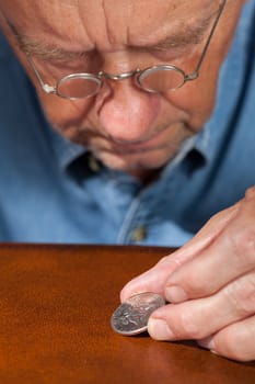 Senior retired caucasian man examining a half dollar coin through magnifying glasses