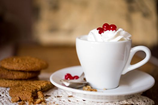 Crumbling oat cookies biscuits with hot coffee and whipped cream with cranberries on top. Shallow DOF