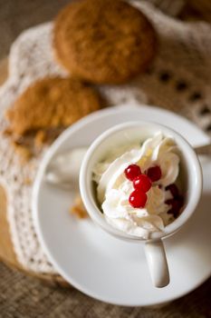 Crumbling oat cookies biscuits with hot coffee and whipped cream with cranberries on top. Shallow DOF