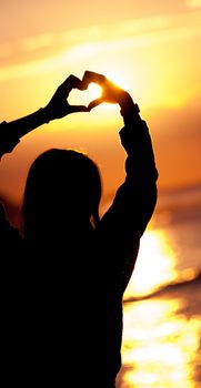 women silhouette makes heart shape sunset