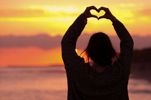 women silhouette makes heart shape sunset