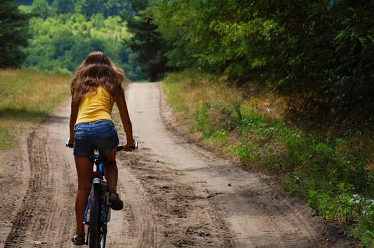 the girl with the bike for a walk in the woods on a sandy road