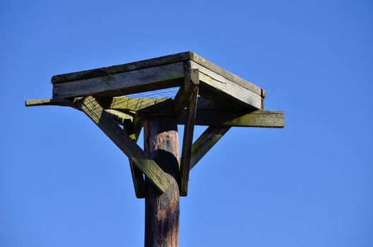 Empty Osprey nest platform against a blue sky.