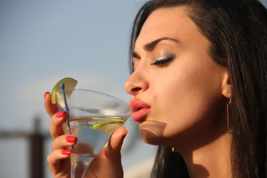 Attractive, young female holding a glass and drinking martini cocktail