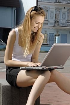 happy blonde collegian using laptop outside educational institution