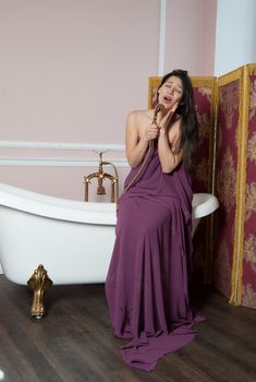 woman in tissue sings in the shower while sitting on the bathtub