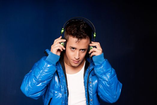 Young man listening music with headphones portrait on blue ligh background