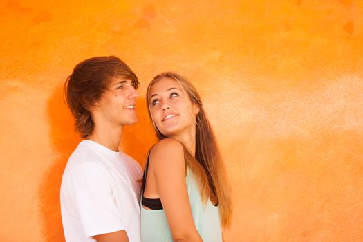 Young beautiful couple having great time over orange background