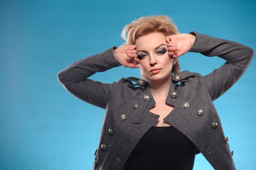 Portrait of beautiful blond femme fatale with shirt hair in gray jacket and black dress posing on blue background