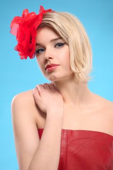 Portrait of beautiful blond woman with a red flower in her hair. Bare shoulders and fashion make-up. On a blue background