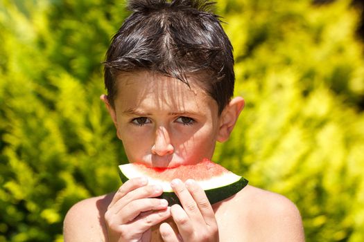 wet boy with watermelon in the garden after swimming