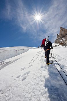 A male climber , dressed in black, climbs up a snowy slope. Winter clear sky day.