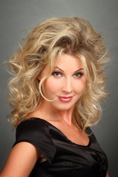 Portrait of the beautiful girl-blonde in a black dress. Looks in the camera .