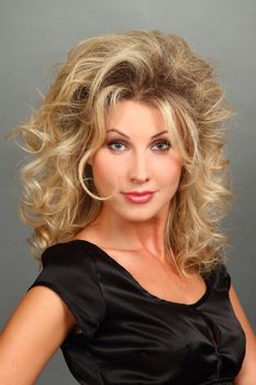 Portrait of the beautiful girl-blonde in a black dress with a magnificent hairdress. Looks in a lens. close up.