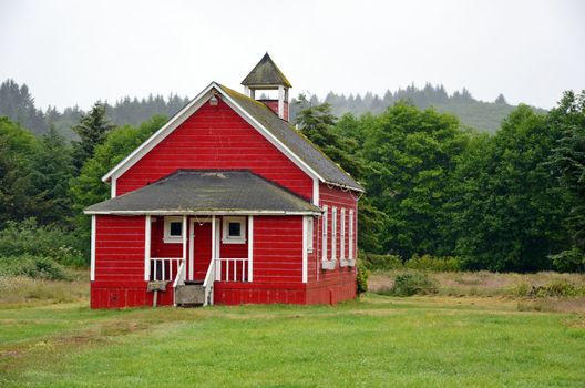 Little red schoolhouse in meadow on misty morning