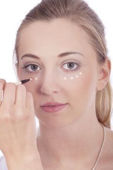 young beautiful woman applying concealer on face isolated