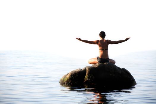 Svelte adult woman doing yoga exercise on the stone in the sea