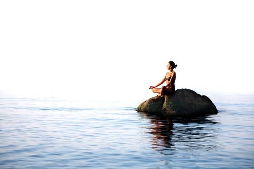 Svelte adult woman sitting in lotus position on the rock in the sea