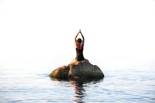 Svelte adult woman doing yoga exercise on the stone in the sea