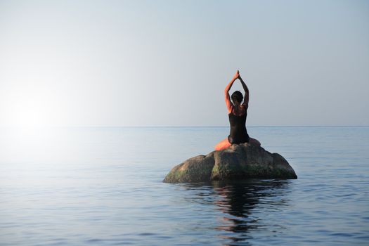 Svelte adult woman doing yoga exercise on the stone in the sea