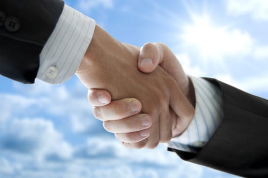 Businessmen shaking hands over blue sky, low angle view.
