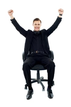 Excited young man sitting on chair with his arms up in excitement