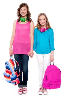 Best friends standing hand in hand and smiling at camera. Holding school bags