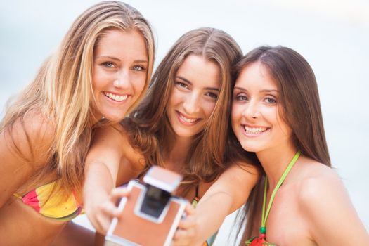 three teenager beautiful girls taking selfie with old camera on the beach