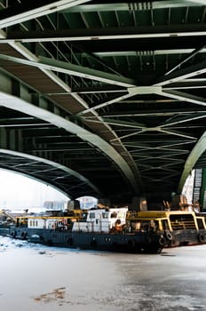 Small tugs under the green bridge at winter, channel is frozen