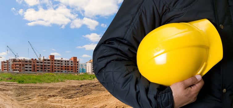 Closeup  of Yellow helmet at builder hands on building background