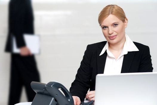 Businesswoman looking at camera while a man walking behind in background