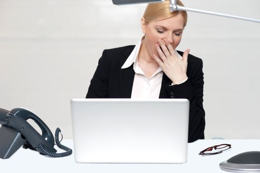 Tried woman sitting with hand on her mouth in front of laptop. It has been a long day at work