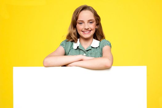Girl posing behind an advertising board isolated against yellow background