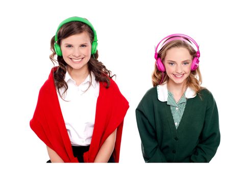 Schoolgirls listening music through headphones isolated over white background