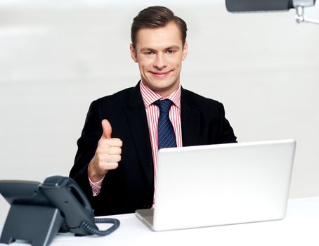 Cheerful businessperson gesturing thumbs up to camera while working in office