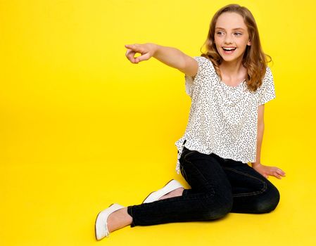 Smiling young girl pointing away. Sitting on floor