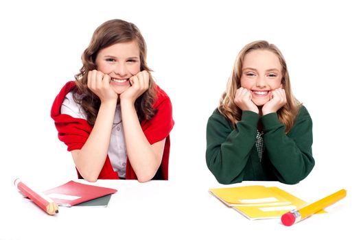 Happy young girls sitting at desk and resting hands on chin isolated on white background