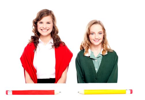 Big pencils lying in front of two school girls. All on white background