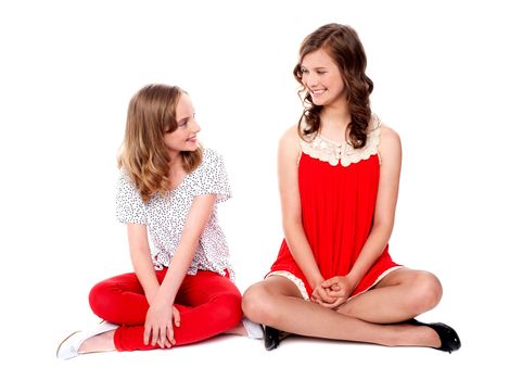 Young cheerful girls sitting together with legs crossed on floor