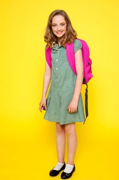 Full length portrait of cheerful school girl standing over yellow background