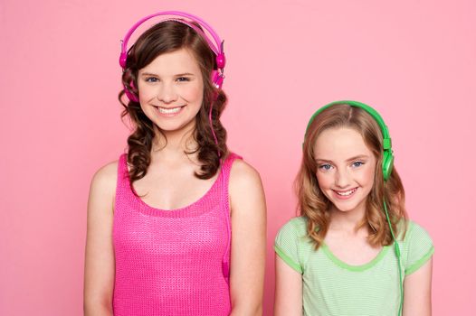 Smiling girls posing with headphone isolated on pink background