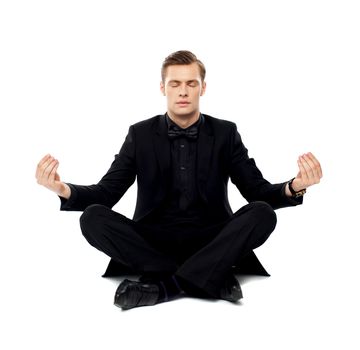 Smart young man in party wear doing yoga. Seated on floor in lotus pose