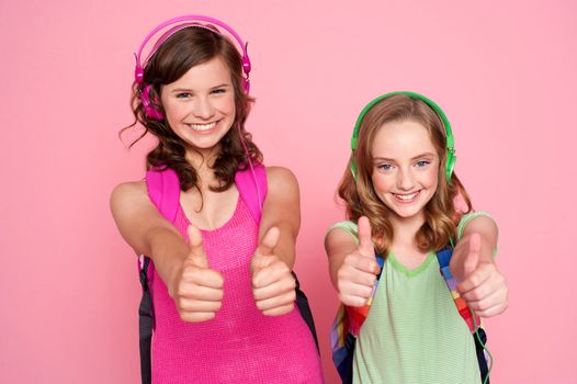 Two beautiful schoolgirls giving thumbs up. Listening to music via headphones as well
