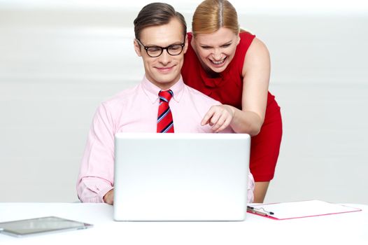 Lady pointing at something funny in laptop while man enjoys too. All on gray background