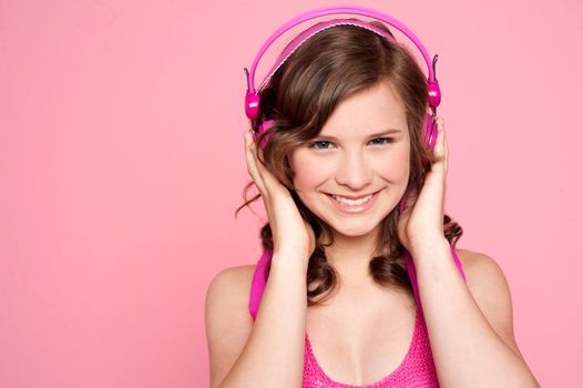 Pretty caucasian girl tuned into music. Holding headphone and looking at camera